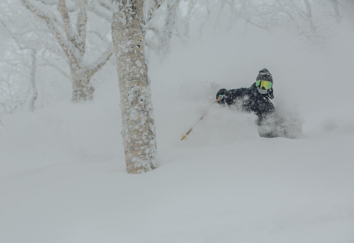 A skier makes a deep turn in powder snow with trees all around