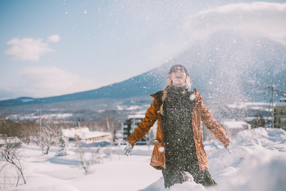 A woman throws a spary of snow above her head with Mount Yotei in the back ground