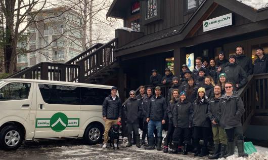A group of Holiday Niseko staff in black jackets with a van to the left