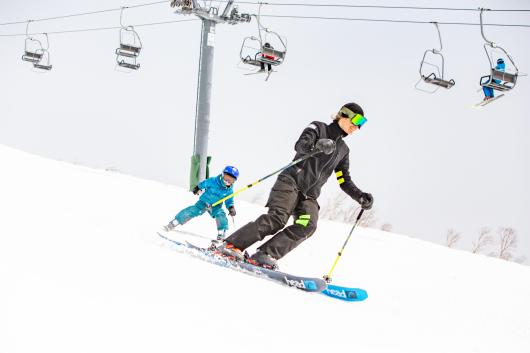 A female ski instructor ski in front of a young child skier