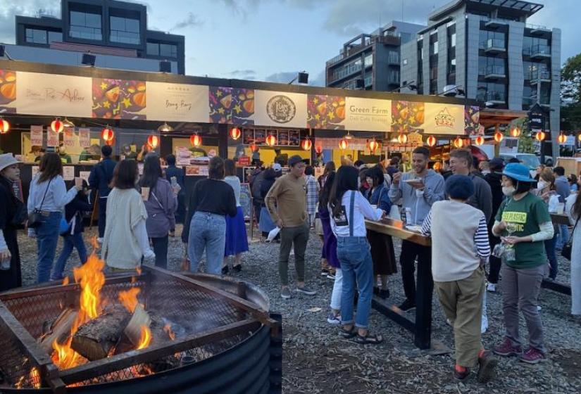 A fire pit and crowd in front of the food stalls.