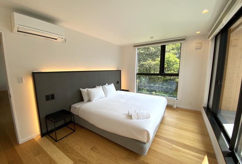 A double bed with back lit head board and greenery visible through the windows.