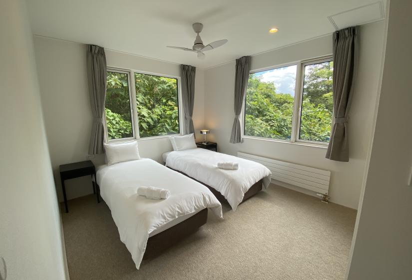 A bedroom with two made up matching single beds and large windows