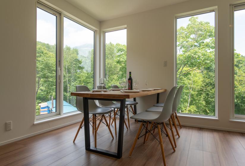 A dining table surrounded by large windows with leafy views