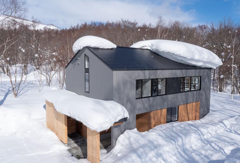 A profile of a two story home with large pillows of snow on the roof.
