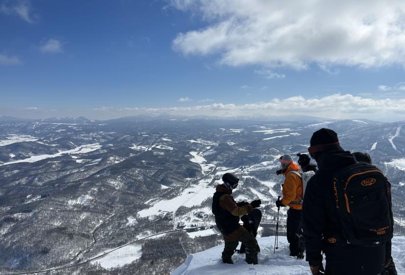 A group of snowboarders on top of a peak with a view to the valley below.