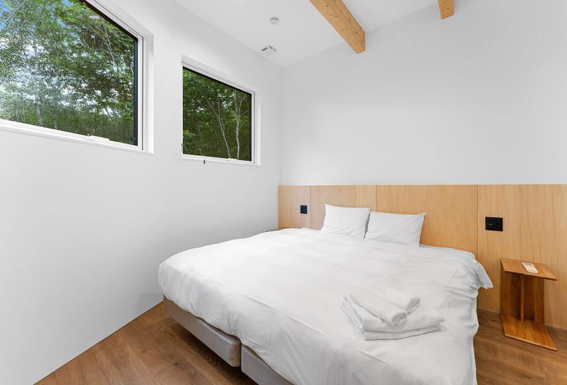 A made white double bed with two windows to the left